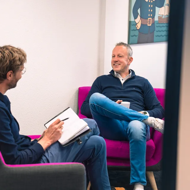 twee mannen aan het overleggen en aan het lachen in roze stoelen